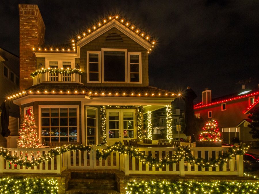 A two-story home lit along every roofline, with garland, lit trees, wrapped columns, and hedge lights