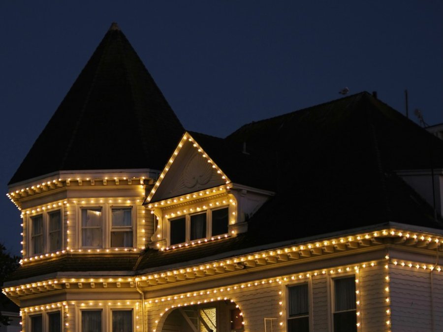 A Victorian house with warm white bulbs outlining the turret, the gable, and every roofline